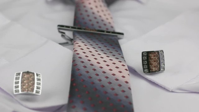 Dolly shot. Close-up knotted pink tie, cufflinks and tie clip on white shirt.