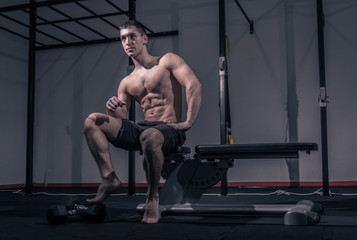 Fototapeta na wymiar one young man, low angle view, bodybuilder muscular sitting posing