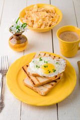 Toast with egg in yellow plate near vase with flower on white wooden background. Healthy breakfast.