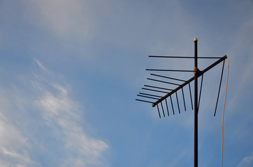 An old and rusty television antenna against a cloudy blue sky