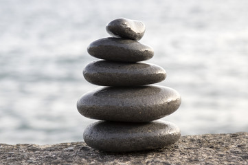 Fototapeta na wymiar Five stones cairn tower, rock zen sculpture, black pebbles and ocean light blue background