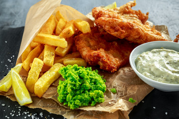 British Traditional Fish and chips with mashed peas, tartar sauce on crumpled paper.