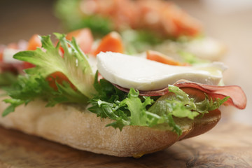 open sandwich with prosciutto, mozzarella and tomatoes on kitchen table, shallow focus