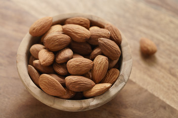 organic almonds in wood bowl on wooden table, shallow focus