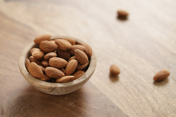 organic almonds in wood bowl on wooden table, shallow focus