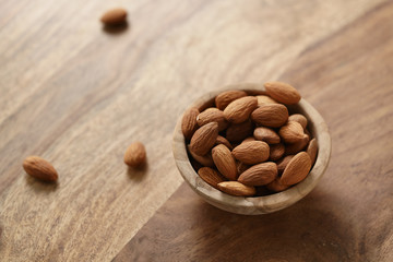 organic almonds in wood bowl on wooden table, shallow focus