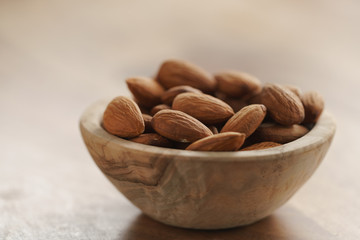 organic almonds in wood bowl on wooden table, shallow focus