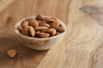 organic almonds in wood bowl on wooden table, shallow focus