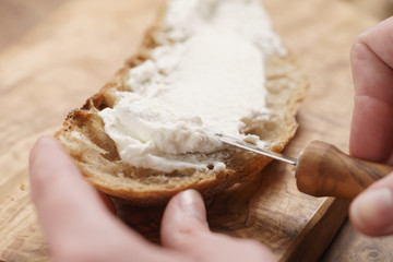 spreading ricotta cheese on fresh rustic bread, shallow focus