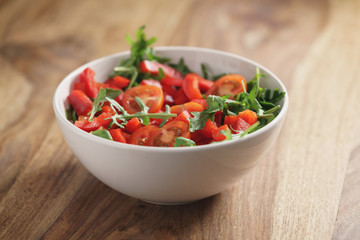 cherry tomatoes with arugula salad in white bowl on wooden table