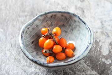 Fresh sea buckthorn on a branch lying on plate, juice. Gray background.