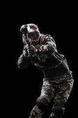 Fototapeta premium Heavily armed masked paintball soldier isolated on black background. Ad concept.