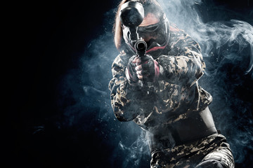 Heavily armed masked paintball soldier isolated on black background. Ad concept. - obrazy, fototapety, plakaty