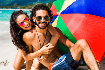 Portraits arabian middle asia man with a European white woman, a married couple on a tropical vacation, in love, sit on the sand, under a bright, colorful sunscreen umbrella, laugh fashion accessories © Nabokov Alex