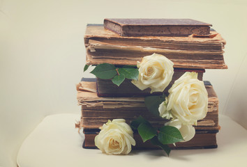 Old books pile with white flowers flowers on white chair background, retro toned