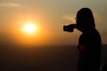 Girl takes a picture on the phone on a coal mine during the sunset