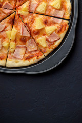 Tasty hawaiian pizza on baking sheet on dark stone background.