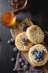 Obraz na płótnie Canvas Hot Home made toasted crumpets served with honey, blueberry. Dark wood background. British breakfast.