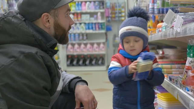 Little child with his father shoping in supermarket and throwing everything off the shelves