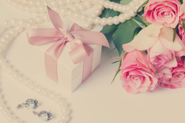 Present box with pink ribbon with jewellery and roses on white table, retro toned
