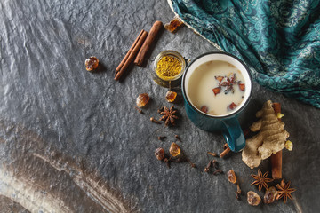 Traditional Indian masala tea in ceramic cup with spices to milk. Dark batskground. Top view. - obrazy, fototapety, plakaty