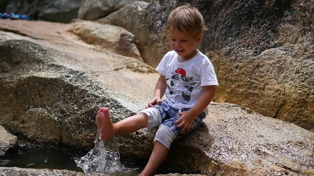 the happy child is sitting on the rocks and making splashes with their feet