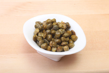 bowl with fresh capers on wooden table