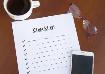 blank checklist on wooden table With coffee, glasses and smartphone