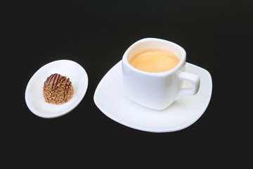 White cup of classic espresso coffee and pralines on black background.