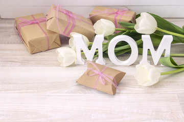Mothers day message with white tulips and gift boxes on white wooden board.