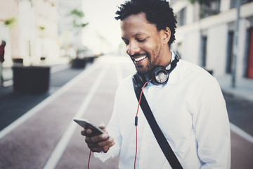 Happy smiling African man using smartphone outdoor.Portrait of young black cheerful man texting a sms message with friends.Blurred background.