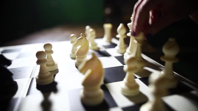 Dolly pull video of the white pieces on a chess board, with shallow depth of field and a hand moving the white queen.