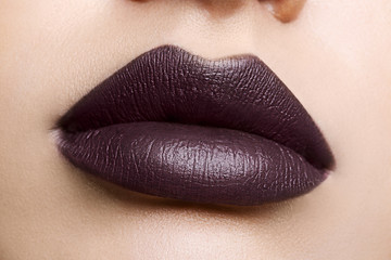 Close up view of beautiful woman lips with purple matt lipstick. Open mouth with white teeth. Cosmetology, drugstore or fashion makeup concept. Beauty studio shot. Passionate kiss