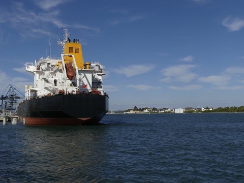 Products Tanker ship discharging at the Oil Terminal of Lorient, France, with black hull and yellow funnel on a sunny day. Horizontal stern view