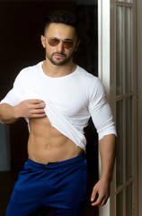 macho man in sunglasses and sportswear showing muscular belly