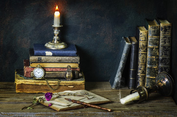 Classic still life with vintage books placed with pocket watch,illuminated candle,letters,inkwell...