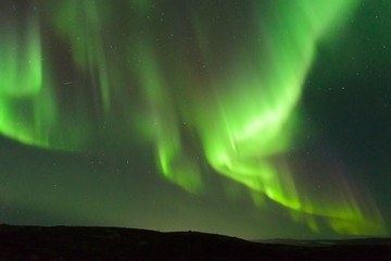 The Aurora in the sky above the hills at night .
