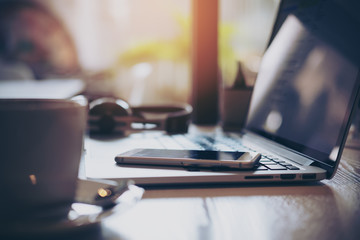 Closeup image of laptop , smart phone , coffee and headphone on wooden table in office