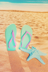 Fototapeta na wymiar Summer beach fun - summer sandals with starfish in beach sand, retro toned