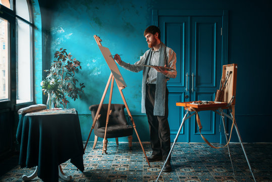 Artist with palette and brush paint on easel