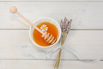Bowl filled with flower honey and spoon with a cup of tea with chamomile flower