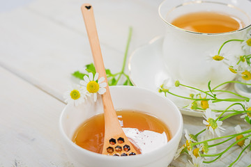 Bowl filled with flower honey and spoon with a cup of tea
