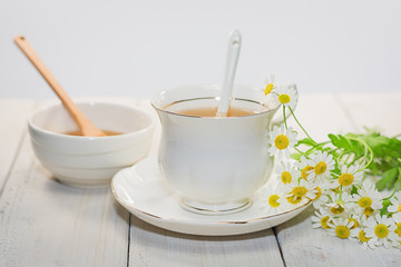Bowl filled with flower honey and spoon with a cup of tea