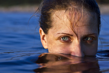 Portrait of young and beautiful woman sitting in the water at the sea. Half of face covered with...