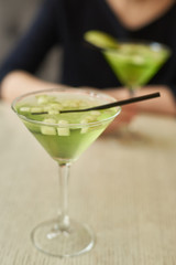 Two glasses of apple martini and apple slices on table in cafe. Young woman blurred at background