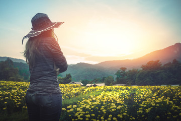 The woman stands on a field of yellow flowers. Sunset atmosphere