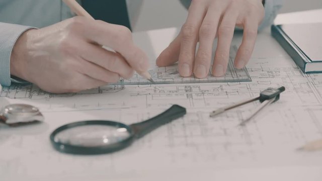 Frellance architect sketching a construction project with pencil and ruler at work place.
