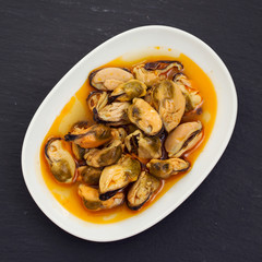 mussels in sauce on white dish on black background