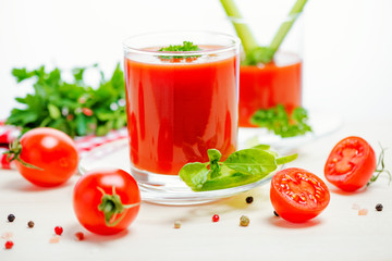 tomato juice in glasses with greenery, basil, cutted tomato fruit and napkin on light wooden background, concept vegetarian food, close up