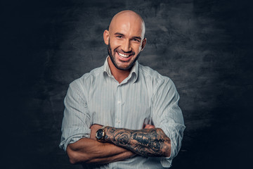 Portrait of shaved head male in a white shirt with tattooed crossed arms.